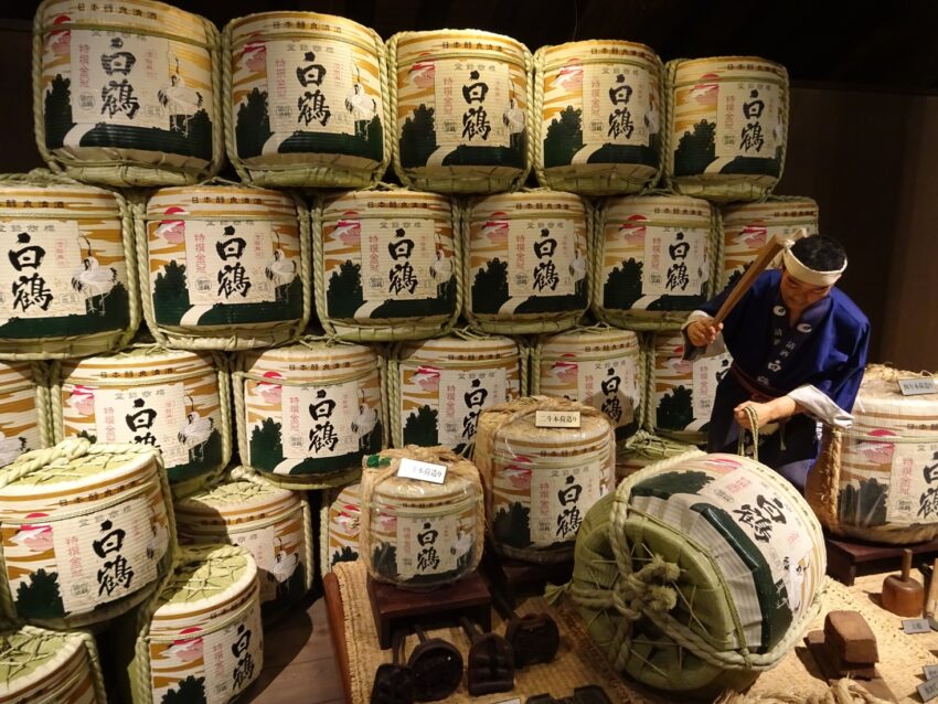 A museum display of sake barrels with a wax figure hammering on one