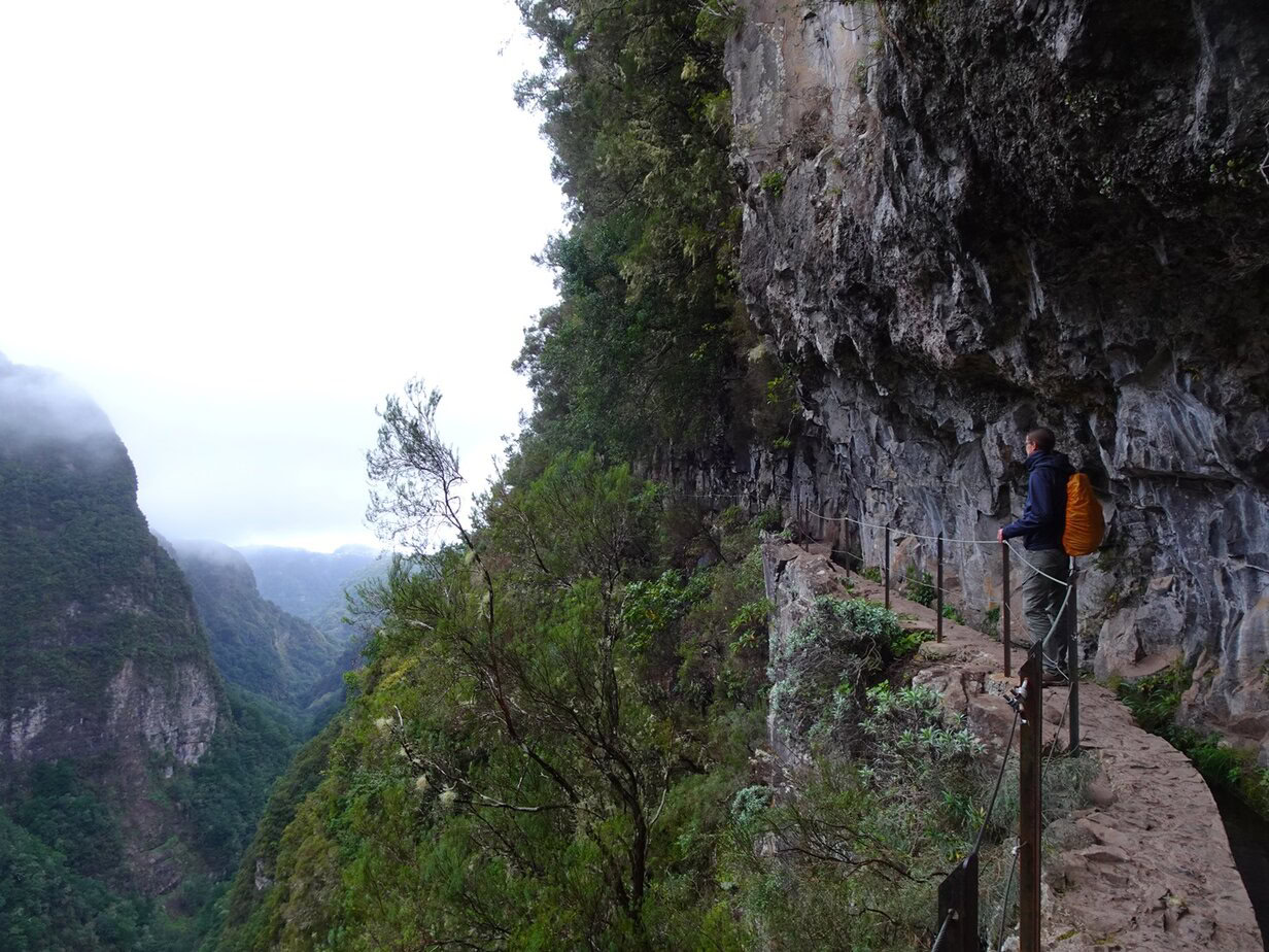 A man standing on a ridge near a cliff looking out over a mountain valley