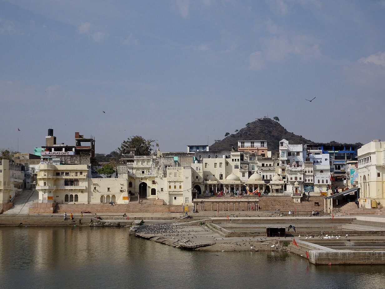 A view of the shore of Pushkar Lake, Rajasthan with ghats, temples, white houses and a wooded hill in the background